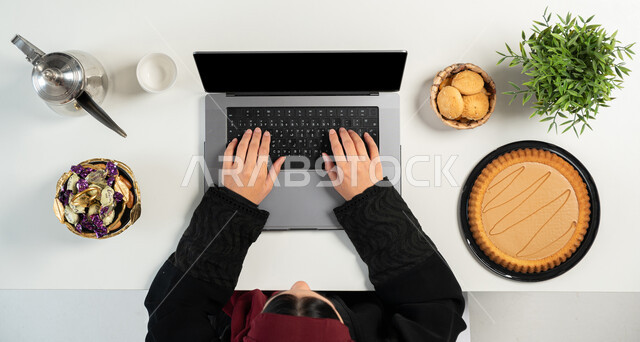 استخدام التقنيات الحديثة، البحث عن الحلويات عن طريق المواقع الالكترونية، بورتريه علوي عامودي ليدي إمرأة عربية خليجية سعودية تستخدم الحاسوب المحمول بجانبها أنواع مختلفة من أطباق الحلو، تشكيلة متنوعة من المأكولات الغنية بالسكريات والسعرات الحرارية، خلفية بيضاء