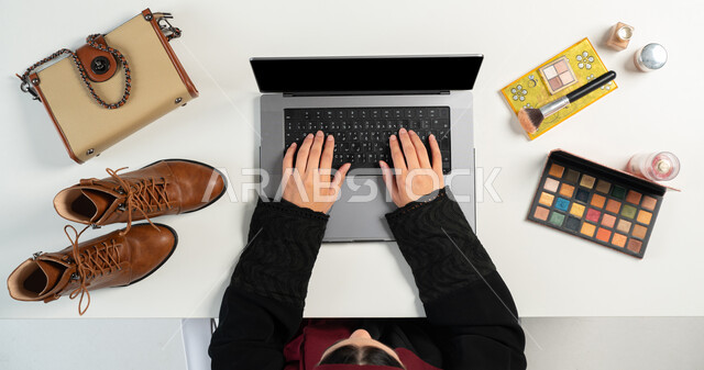 مفهوم التسوق الإلكتروني، الحصول على الأغراض الشخصية ومستحضرات التجميل عن طريق الأونلاين، الطلب عبرالمواقع الإلكترونية، البيع والشراء عبر الانترنت، بورتريه علوي عامودي ليدي إمرأة عربية خليجية سعودية تقوم باستخدام الحاسوب المحمول، خلفية بيضاء