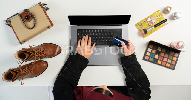 البيع والشراء عبر الانترنت، الطلب عبر المواقع الإلكترونية، مفهوم التسوق الإلكتروني، بورتريه علوي عامودي ليدي إمرأة عربية خليجية سعودية تقوم باستخدام الحاسوب المحمول، الدفع عبر البطاقة البنكية، الحصول على الملابس ومستحضرات التجميل عن طريق الأونلاين، خلفية بيضاء