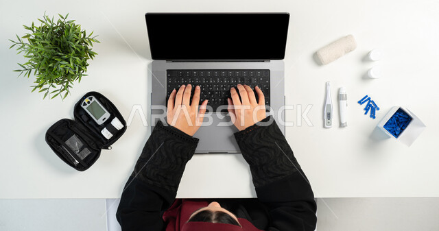 Office women's jobs and professions, e-clinic concept, online medical consultations, vertical top portrait of a Saudi Arabian Gulf woman using a laptop, getting medical equipment and supplies online, blank black screen display, white background