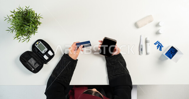 استخدام البطاقة البنكية الحصول على الأجهزة والمستلزمات الطبية أونلاين، مفهوم العيادة الالكترونية، الاستشارات الطبية عبر المواقع الإلكترونية، بورتريه علوي عامودي لإمرأة عربية خليجية سعودية تقوم باستخدام الهاتف المحمول، عرض شاشة سوداء فارغة، خلفية بيضاء