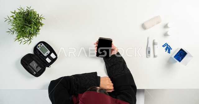 مفهوم العيادة الالكترونية، الاستشارات الطبية عبر المواقع الإلكترونية، بورتريه علوي عامودي لإمرأة عربية خليجية سعودية تقوم باستخدام الهاتف المحمول، الحصول على الأجهزة والمستلزمات الطبية أونلاين، عرض شاشة سوداء فارغة، خلفية بيضاء
