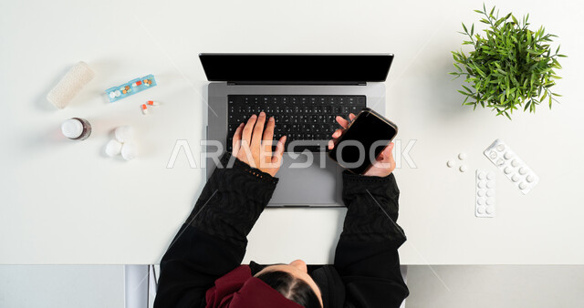 الحصول على الأدوية من خلال الانترنت، بورتريه علوي عامودي ليدي إمرأة عربية خليجية سعودية تقوم باستخدام الهاتف المحمول و جهاز الحاسوب لشراء الدواء من الصيدلية الإلكترونية، الحصول على المستحضرات الطبية أونلاين، عرض شاشة سوداء فارغة، خلفية بيضاء