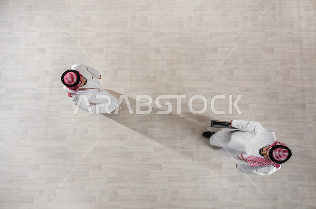 الانجاز والانتهاء من الدوام, بورتريه علوي عامودي لزملاء عمل عرب خليجيين سعوديين يرتديان الثوب التقليدي والشماغ, خروج الموظفين عند انتهاء أوقات الدوام الرسمية, المتعة مع الأصدقاء, التجول في ممرات الشركة, قضاء أوقات ممتعة في العمل, خلفية بيج