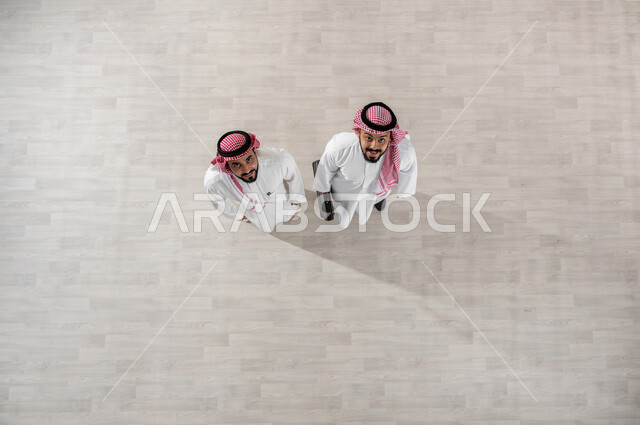 النظر الى الكاميرا بإيماءات السرور, بورتريه علوي عامودي لزملاء عمل عرب خليجيين سعوديين يرتديان الثوب التقليدي والشماغ, خروج الموظفين عند انتهاء أوقات الدوام الرسمية, المتعة مع الأصدقاء, التجول في ممرات الشركة, قضاء أوقات ممتعة في العمل, خلفية بيج