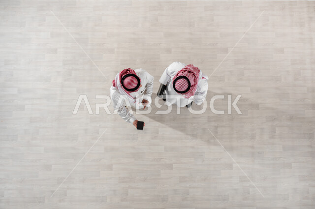 النظر الى الهاتف المحمول, بورتريه علوي عامودي لزملاء عمل عرب خليجيين سعوديين يرتديان الثوب التقليدي والشماغ, خروج الموظفين عند انتهاء أوقات الدوام الرسمية, استخدام التقنيات والتكنولوجيا الحديثة, التجول في ممرات الشركة, قضاء أوقات ممتعة في العمل, خلفية بيج
