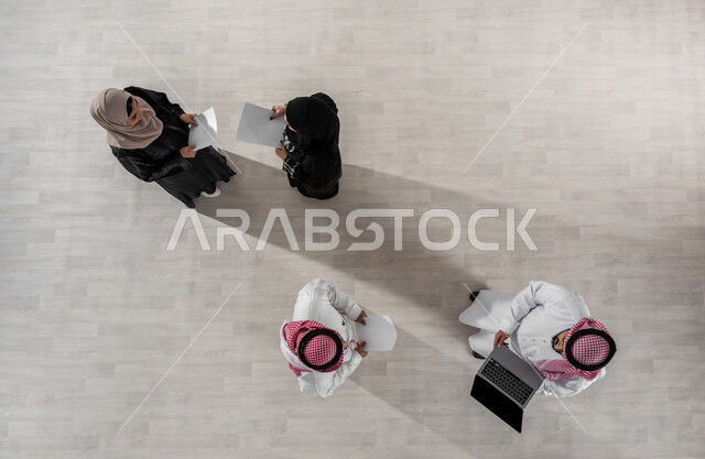 بيئة العمل السعودي, الحوارات والنقاشات ضمن الفريق, مفهوم الشراكة والتعاون, بورتريه علوي عامودي لموظفين عرب سعوديين خليجيين في اجتماع, ارتداء اللباس السعودي التقليدي, النجاح وتحقيق الاهداف, استخدام الاجهزة والتقنيات الحديثة لإنجاز الاعمال المكتبية, خلفية بيج