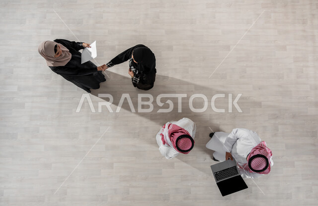 مفهوم الشراكة والتعاون, الحوارات والنقاشات ضمن الفريق, بيئة العمل السعودي, بورتريه علوي عامودي لموظفين عرب سعوديين خليجيين في اجتماع, ارتداء اللباس السعودي التقليدي, النجاح وتحقيق الاهداف, استخدام الاجهزة والتقنيات الحديثة لإنجاز الاعمال المكتبية, خلفية بيج