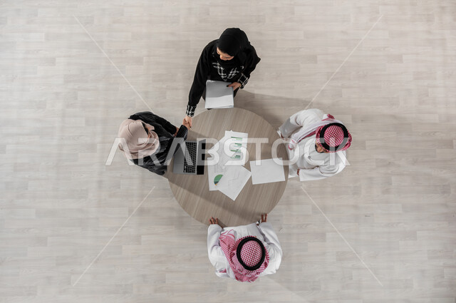 Explanation of the required tasks, comfortable work environment in the company, organizing and managing the work concept schedule, cooperation and understanding between the team, exchange of experiences and successful agreements, vertical overhead portrait of Saudi Gulf Arab co-workers in a meeting, wearing traditional Saudi dress, beige background