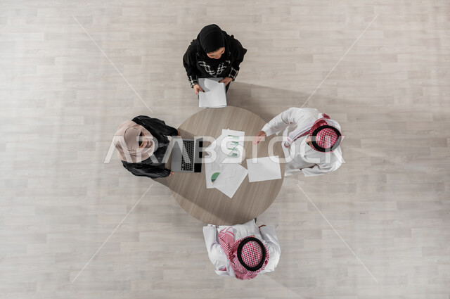 تنظيم وادارة جدول مفهوم العمل, بيئة العمل المريحة في الشركة, شرح المهام المطلوبة بسعادة وحب, التعاون والتفاهم بين الفريق, تبادل الخبرات والاتفاقيات الناجحة, بورتريه علوي عامودي لموظفين عرب خليجيين سعوديين في اجتماع, ارتداء اللباس السعودي التقليدي, خلفية بيج