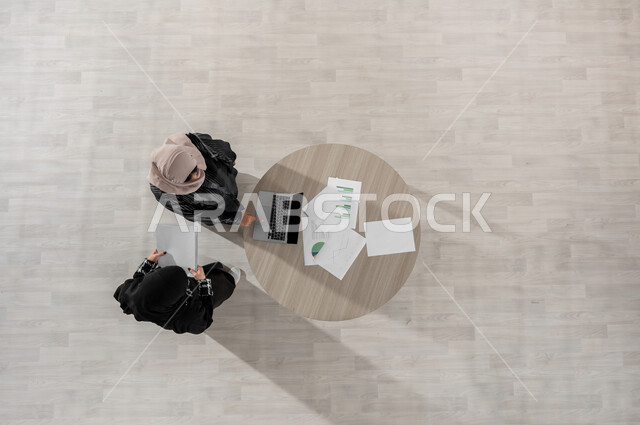 المساعدة و تبادل الخبرات والاتفاقيات الناجحة, التعاون والتفاهم بين الفريق, بورتريه علوي عامودي لسيدتين عربيتين خليجيتين سعوديتين في اجتماع عمل, ارتداء اللباس السعودي التقليدي, بيئة العمل المريحة في الشركة السعودية, دمج التكنولوجيا في الحياة  العملية, خلفية بيج