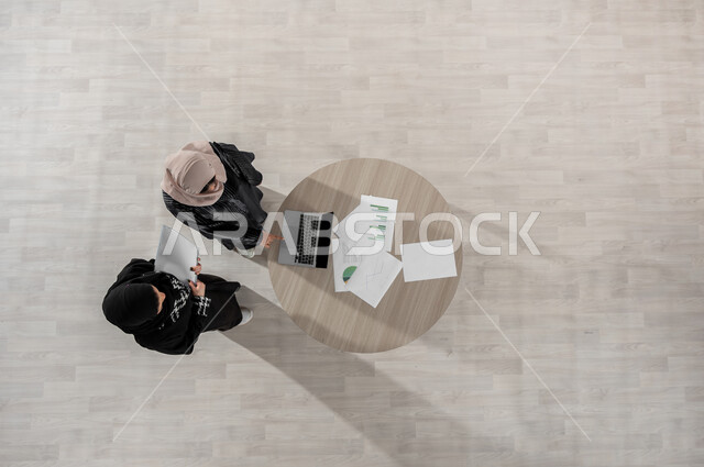 تبادل الخبرات والاتفاقيات الناجحة, التعاون والتفاهم بين الفريق,  بورتريه علوي عامودي لسيدتين عربيتين خليجيتين سعوديتين في اجتماع عمل, ارتداء اللباس السعودي التقليدي, بيئة العمل المريحة في الشركة السعودية, دمج التكنولوجيا في الحياة  العملية, خلفية بيج