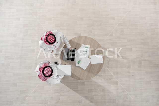 دمج التكنولوجيا بالعمل، التفاعل الجماعي لتحقيق أهداف الشركة وحل المشكلات، مفهوم الإدارة المتعاونة، بورتريه علوي عامودي لموظفين عربيين خليجيين سعوديين يرتديان الشماغ والثوب التقليدي، المناقشة في أمور العمل باستخدام الأوراق والبيانات، خلفية بيج