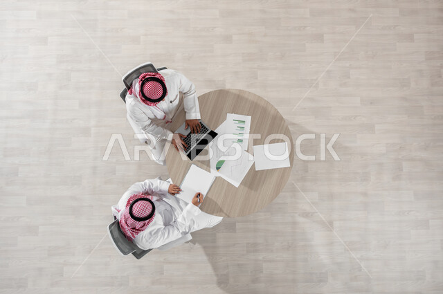 التفاعل الجماعي لتحقيق أهداف الشركة وحل المشكلات، مفهوم الإدارة المتعاونة، بورتريه علوي عامودي لموظفين عربيين خليجيين سعوديين يرتديان الشماغ والثوب التقليدي، المناقشة في أمور العمل باستخدام الأوراق والبيانات، دمج التكنولوجيا بالعمل، خلفية بيج