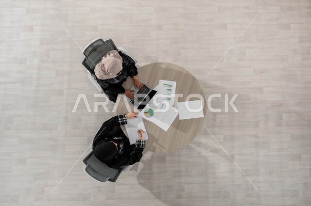 التفاهم و التعاون بين زملاء العمل , بورتريه علوي عامودي لامرأتان عربيتان خليجيتان سعوديتان ترتديان الزي التقليدي , بيئة العمل في السعودية , تبادل الأفكار و الخبرات  , عرض شاشة سوداء فارغة عبر الحاسوب , خلفية بيج