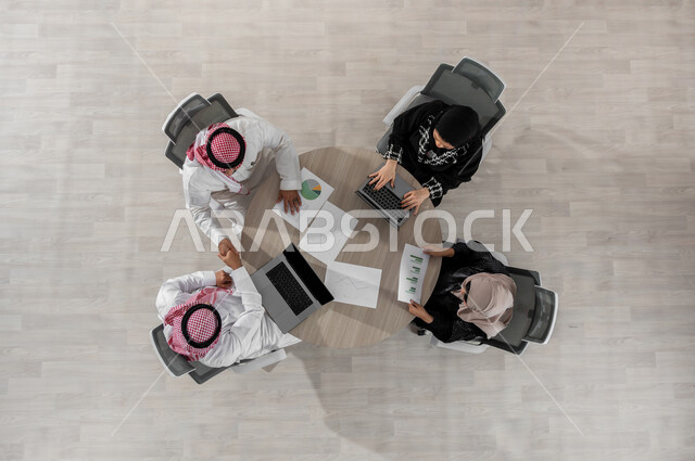 اجتماع عمل لمناقشة أهداف المشاريع , بورتريه علوي عامودي لفريق عمل عربي خليجي سعودي يرتدون الزي التقليدي , شرح و تقسيم المهام , مفهوم التعاون و المشاركة , عرض شاشة سوداء عبر الحاسوب , خلفية بيج