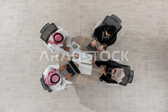 استخدام الحاسب المحمول في العمل , بورتريه علوي عامودي لفريق عمل عربي خليجي سعودي يرتدون الزي التقليدي , اجتماع عمل لشرح و تحليل البيانات , تطوير المشاريع و الاستثمارات, عرض شاشة سوداء عبر الحاسوب , خلفية بيج