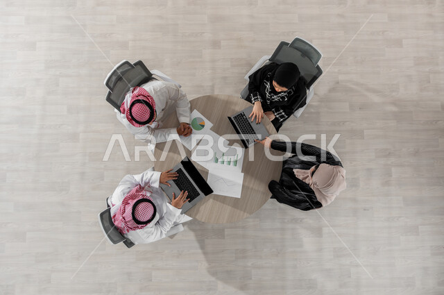اجتماع عمل لشرح و تقسيم المهام , بورتريه علوي عامودي لفريق عمل عربي خليجي سعودي يرتدون الزي التقليدي , دمج التكنولوجيا بالعمل , تبادل الأفكار و الخبرات , عرض شاشة سوداء عبر الحاسوب , خلفية بيج