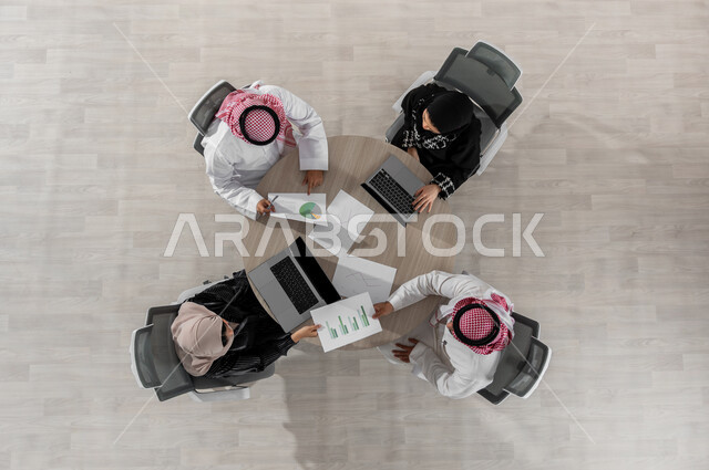 دراسة و تحليل الرسوم البيانية لأرباح الشركة  , تقسيم المهام بين الموظفين , بورتريه علوي عامودي لفريق عمل عربي خليجي سعودي يرتدون الزي التقليدي , اجتماع عمل لتطوير المشاريع و الاستثمارات , عرض شاشة سوداء عبر الحاسوب , خلفية بيج