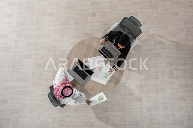 شرح و تحليل الرسوم البيانية , بورتريه علوي عامودي لرجل و سيدة أعمال عربيان خليجيان سعوديان يرتديان الزي التقليدي , تبادل الخبرات و المعلومات , عرض شاشة سوداء عبر الحاسوب , خلفية بيج