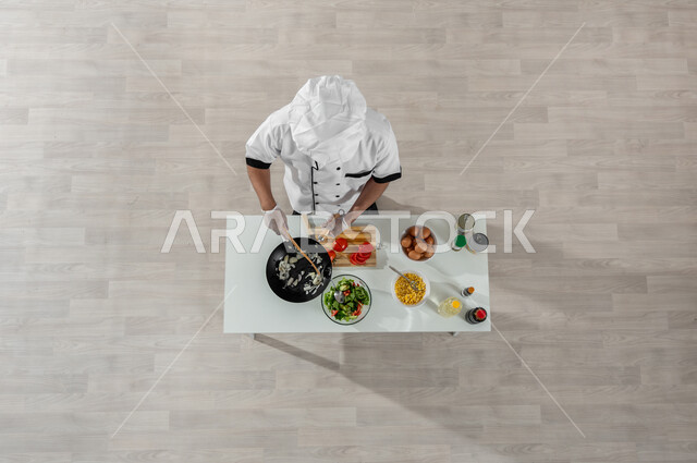 فنون ومهارات الطبخ، بورتريه علوي عامودي لشيف عربي خليجي سعودي يرتدي يونيفورم الطبخ  ويقوم بتجهيز وإعداد الطعام وأمامه المكونات والمقادير المناسبة، تجهيز وجبة صحية ولذيذة، اكتساب خبرات جديدة، خلفية بيج