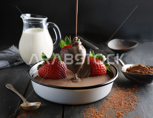 سقوط الشوكولا على حبات ناضجة من فاكهة الفراولة اللذيذة على سطح خشبي، مشروب الحليب الصحي المفيد في اناء زجاجي, محاصيل ومنتجات محلية زراعية سعودية, فواكه موسميه طازجه ،خلفية سوداء