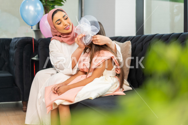 A wonderful sharing of a mother with her daughter on the morning of Eid, wearing the traditional Saudi dress, Eidiya, and Gergean