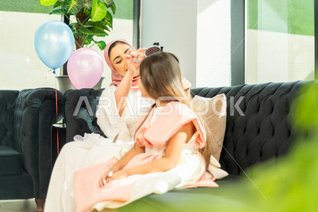 A wonderful sharing of a mother with her daughter on the morning of Eid, wearing the traditional Saudi dress, Eidiya, and Gergean