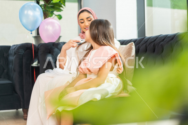 A wonderful sharing of a mother with her daughter on the morning of Eid, wearing the traditional Saudi dress, Eidiya, and Gergean