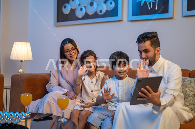 مفهوم الترابط الأسري، تعابير السعادة والسرور، متابعة الافلام والمسلسلات باستخدام التابلت، اجراء مكالمات فيديو مع الاقارب،  أجواء اسرية سعيدة في المنزل، زوجان عربيان خلجيان سعوديان يقومان بشرب العصير برفقه ابنائهما، قضاء اوقات عائلية ممتعة