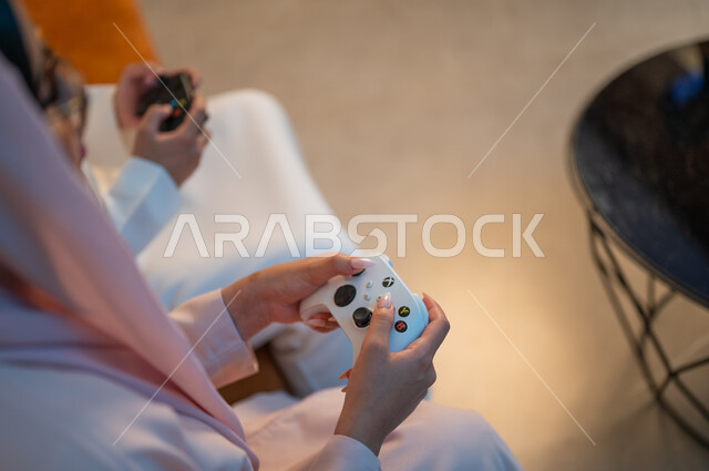 فعاليات عطلة نهاية الأسبوع، تقنيات الكترونية حديثة ترفيهيه, قضاء وقت ممتع ومسلي في المنزل، التفاعل والاندماج مع ألعاب الفيديو، زوجان عربيان خليجيان سعوديان يمسكان عصا التحكم بتعابير السرور والسعادة