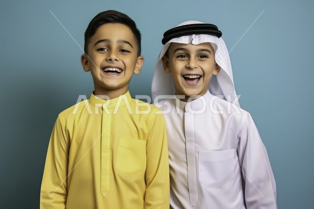 الاهتمام بالأناقة والمظهر الخارجي، مشاعر الحب بين الاخوة, بورتريه مقرب لصديقين عربيين خليجين سعوديين مبتسميين يرتديان الزي التقليدي ينظران الى الكاميرا بإيماءات السرور، التقاط الصور الشخصية، خلفية زرقاء