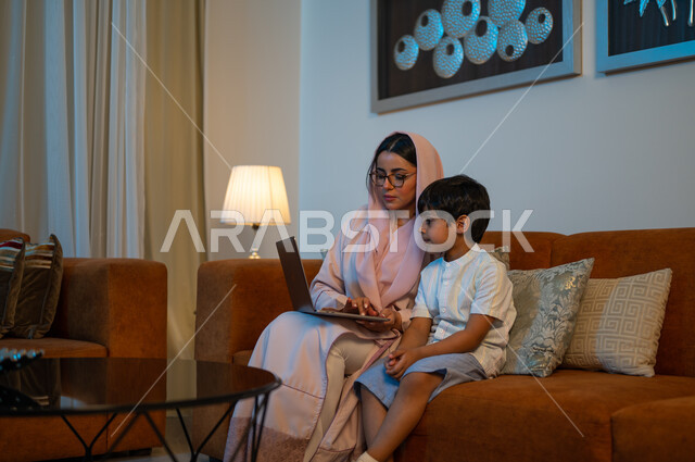 معلمة خصوصي لمتابعة الدروس في المنزل، أم عربية خليجة سعودية محجبة تقوم بتعليم وتدريس ابنها باستخدام الحاسب المحمول، متابعة منصات التعليم الالكتروني المتاحة عبر الانترنت، دمج التعليم مع التقنية و التكنولوجيا، حل الواجبات المنزليه