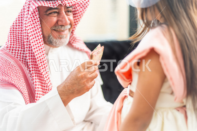 تقديم العيدية للأطفال في عيد الفطر المبارك ، أجواء رائعة لعائلة سعودية داخل المنزل تحتفل بعيد الفطر السعيد ، عيد فطر مبارك ،  الزيارات العائلية وتجمعات الأسر ،  تقديم العيديات و الحلوى ، القرقيعان