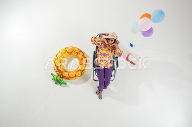 إيماءات الفرح و السعادة بقضاء العطلة على الشاطئ , بورتريه علوي عامودي لامرأة عربية خليجية سعودية ترتدي ملابس الشاطئ الصيفية و قبعة من القش , فعاليات و رحلات صيفية , خلفية بيضاء