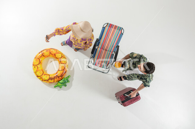 استخدام الهاتف المحمول لالتقاط الصور , امرأة تأخذ سيلفي مع زوجها , بورتريه علوي عامودي لزوجان عربيان خليجيان سعوديان يرتديان ملابس الشاطئ الصيفية , الاستمتاع بالإجازة على الشاطئ , خلفية بيضاء