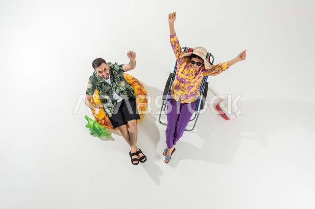 A fun summer trip, looking at the camera with gestures of enthusiasm and joy, a vertical overhead portrait of a Saudi Gulf Arab couple wearing summer beach clothes, enjoying refreshing summer drinks, white background