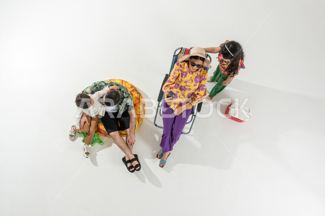 مشاركة الأسرة الأوقات الممتعة , أم تلتقط صورة مع ابنتها عبر الجوال , بورتريه علوي عامودي لعائلة عربية خليجية سعودية يرتدون ملابس الشاطئ الصيفية , أجواء عائلية سعيدة , خلفية بيضاء