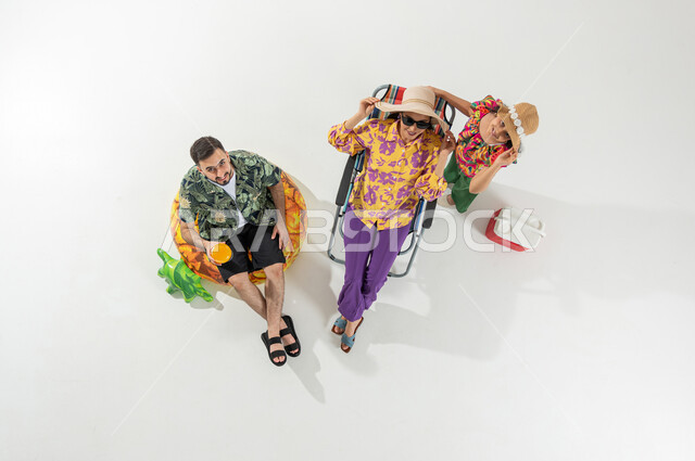 الاستمتاع بعطلة الصيف , شرب العصائر المنعشة , بورتريه علوي عامودي لعائلة عربية خليجية سعودية يرتدون ملابس الشاطئ الصيفية , النظر إلى الكاميرا بإيماءات الفرح و السرور , خلفية بيضاء