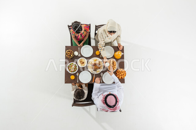 The joy of breaking the fast with the family in the month of Ramadan, a vertical overhead portrait of a Saudi Gulf Arab family wearing traditional dress sitting at the dining table, a happy Ramadan atmosphere, a variety of foods, a white background