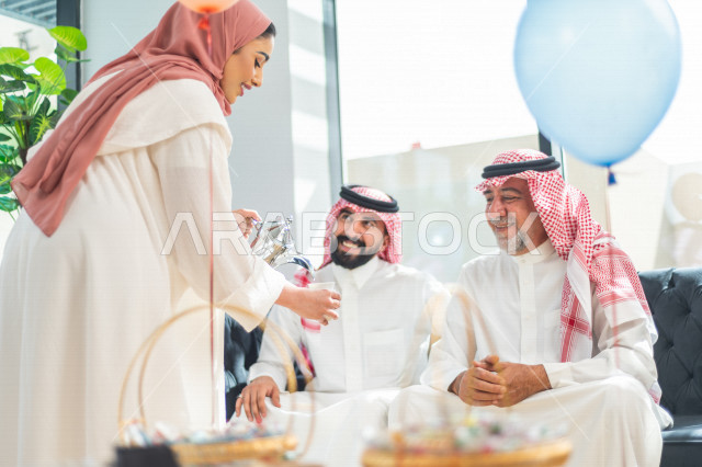 مرأه عربية سعودية تقوم بتقديم القهوه العربية على العائلة ، مشاركة لأجواء رائعة لعائلة سعودية داخل المنزل تحتفل بعيد الفطر السعيد ، عيد فطر مبارك ،  الزيارات العائلية وتجمعات الأسر