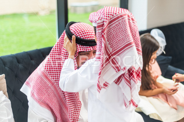A happy Saudi Arabian Gulf child, wearing elegant Eid clothes, kisses his grandfather and congratulates him on the coming of Eid, the celebration of Happy Eid al-Fitr, the blessed Eid al-Fitr