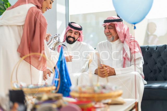 مرأه عربية سعودية تقوم بتقديم القهوه العربية على العائلة ، مشاركة لأجواء رائعة لعائلة سعودية داخل المنزل تحتفل بعيد الفطر السعيد ، عيد فطر مبارك ،  الزيارات العائلية وتجمعات الأسر