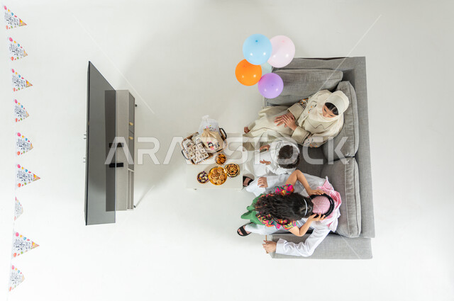 أعياد و مناسبات إسلامية , فتاة تقبل رأس والدها , بورتريه علوي عامودي لعائلة عربية خليجية سعودية يرتدون الثوب التقليدي يجلسون على الأريكة في غرفة المعيشة , الاحتفال مع العائلة بقدوم العيد , عرض شاشة سوداء فارغة عبر التلفاز , خلفية بيضاء