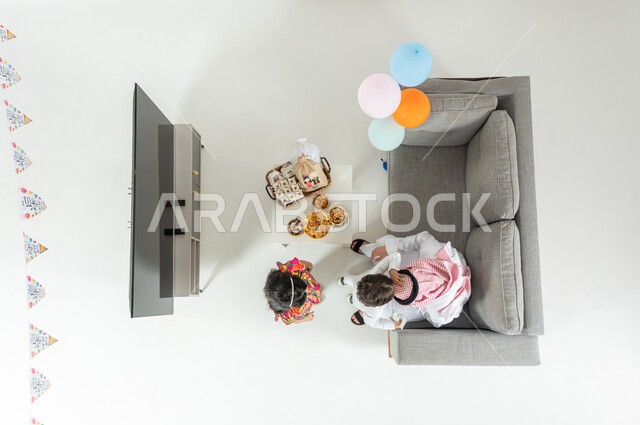 التهنئة بقدوم العيد ,ولد يقبل رأس والده  , بورتريه علوي عامودي لأب عربي خليجي سعودي يرتدي الزي التقليدي و الشماغ مع أبنائه يجلس على الأريكة في غرفة المعيشة , أجواء عائلية سعيدة , عرض شاشة سوداء فارغة عبر التلفاز , خلفية بيضاء