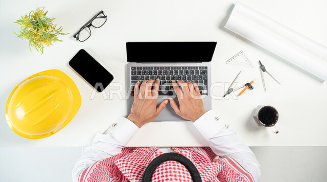 استخدام المواقع الالكترونية للبحث عن مستلزمات البناء، بورتريه مقرب ليدي رجل عربي خليجي سعودي يستخدم جهاز الحاسوب المحمول وبجانبه فنجان من القهوة والجوال وأدوات هندسية، البيع والشراء عبر الانترنت، هندسة المباني بطرق عصرية، خلفية بيضاء