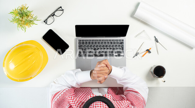 استخدام المواقع الالكترونية للبحث عن مستلزمات البناء، بورتريه مقرب ليدي رجل عربي خليجي سعودي يستخدم جهاز الحاسوب المحمول وبجانبه جوال وأدوات هندسية وفنجان من القهوة، البيع والشراء عبر الانترنت، ايماءات الإنجاز والفرح، عرض شاشة سوداء فارغة، خلفية بيضاء