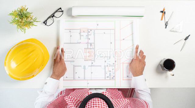 Reviewing and implementing construction projects, obtaining building supplies, a close-up portrait of a Saudi Gulf Arab man holding an engineering plan in his hand, engineering tools and a cup of coffee next to him, engineering buildings in modern ways, a white background