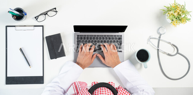 طلب استشارات طبية  أونلاين، البيع والشراء من خلال استخدام المواقع الالكترونية، بورتريه مقرب ليدي رجل عربي خليجي سعودي يستخدم جهاز الحاسوب المحمول وبجانبه دفتر اسشارات طبية وفنجان من القهوة وسماعات الفحص الطبي، عرض شاشة سوداء فارغة، خلفية بيضاء