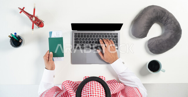 بيع وشراء وقطع تذاكر الطيران أونلاين، استخدام المواقع الالكترونية للبحث عن رحلات جوية، بورتريه مقرب ليدي رجل عربي خليجي سعودي يستخدم جهاز الحاسوب المحمول وبيده تذكرة وجواز السفر وبجانبه فنجان من القهوة ومجسمات مصغرة للطائرات، عرض شاشة سوداء فارغة، خلفية بيضاء